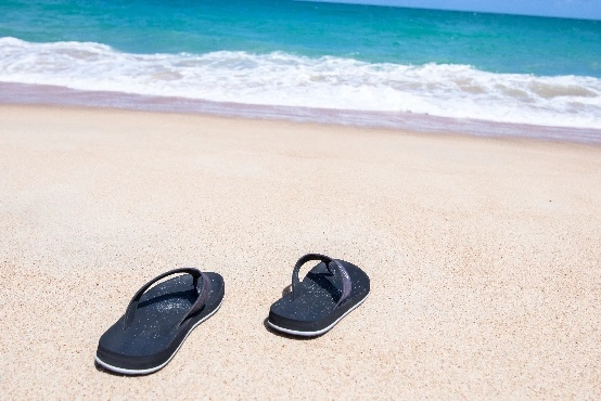 Twee slippers aan het strand. Je kan de zee verderop zien.