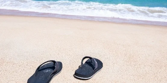 Twee slippers aan het strand. Je kan de zee verderop zien.