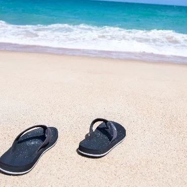 Twee slippers aan het strand. Je kan de zee verderop zien.